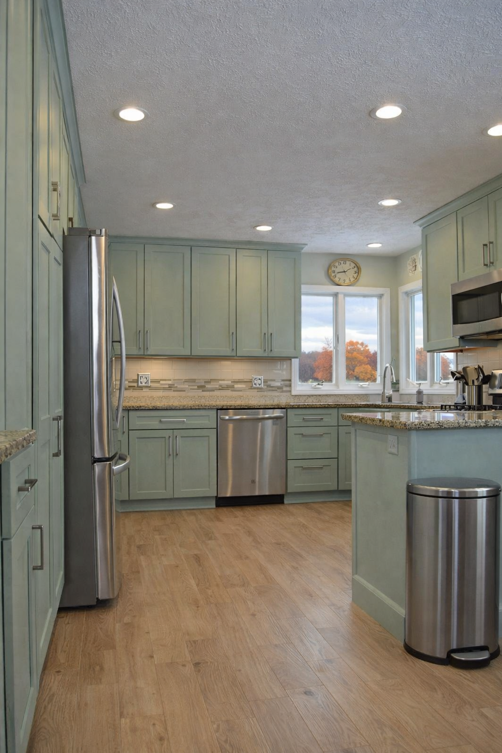 A modern kitchen with fresh sage cabinets with beige granite countertops and light oak flooring