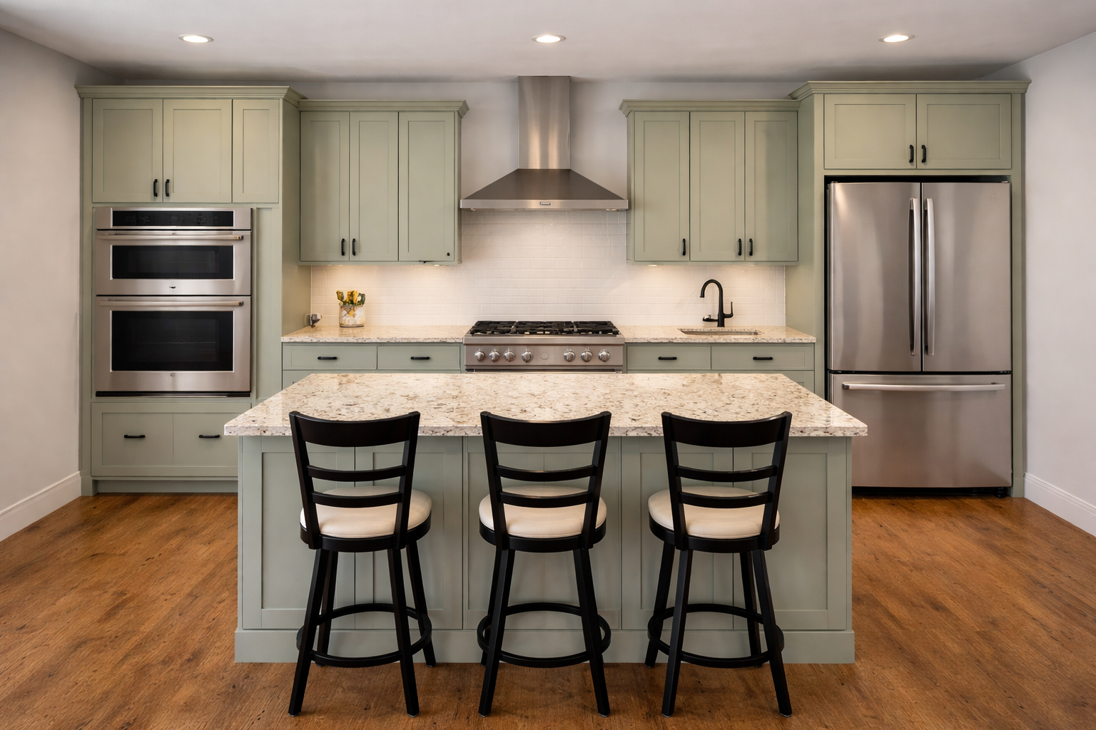 Quaint fresh sage color cabinets in a linear layout with black hardware on doors and drawers, large kitchen island and granite countertops