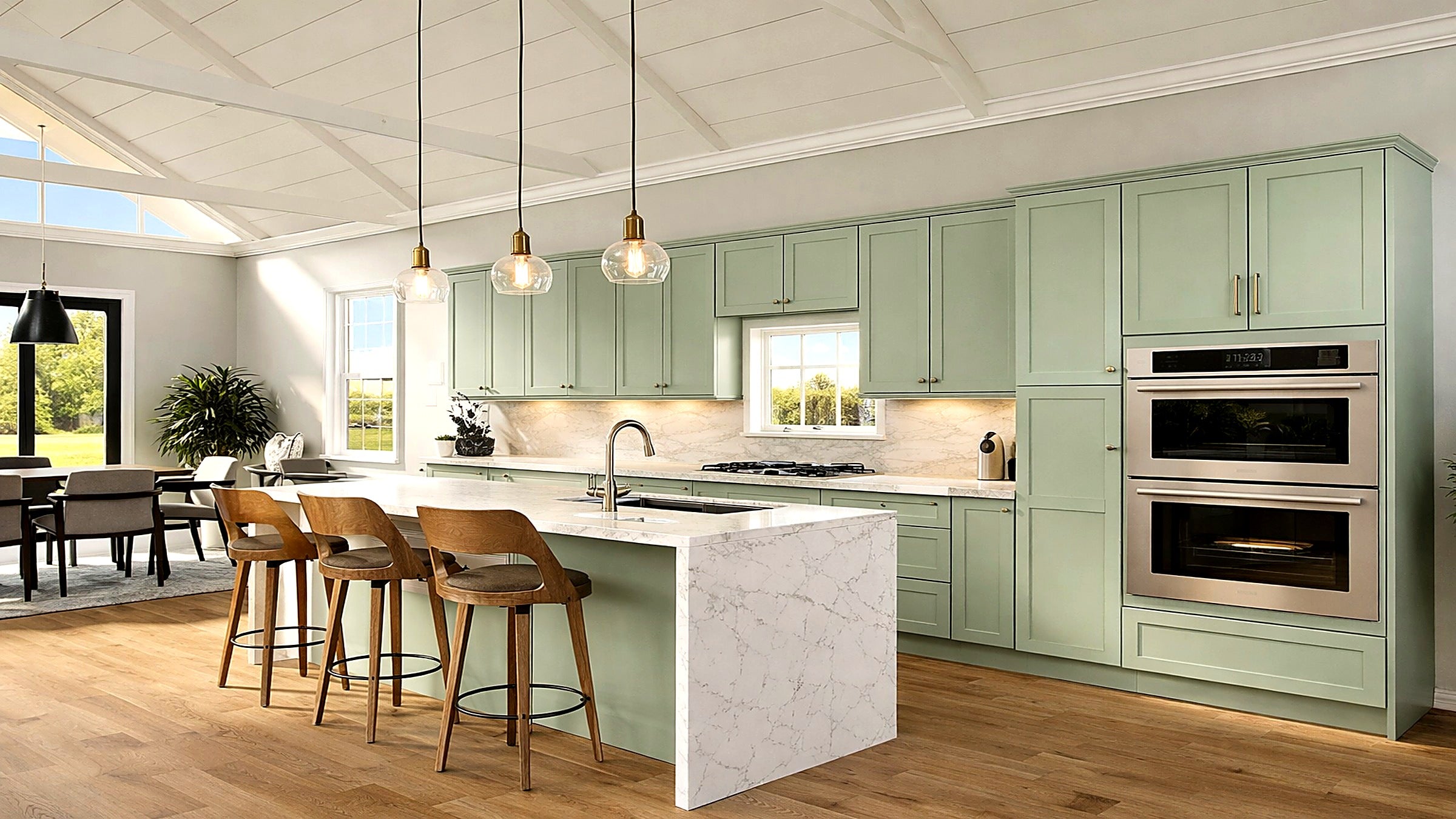 Sage green kitchen cabinets in a linear layout with antique brass accents and wooden barstools