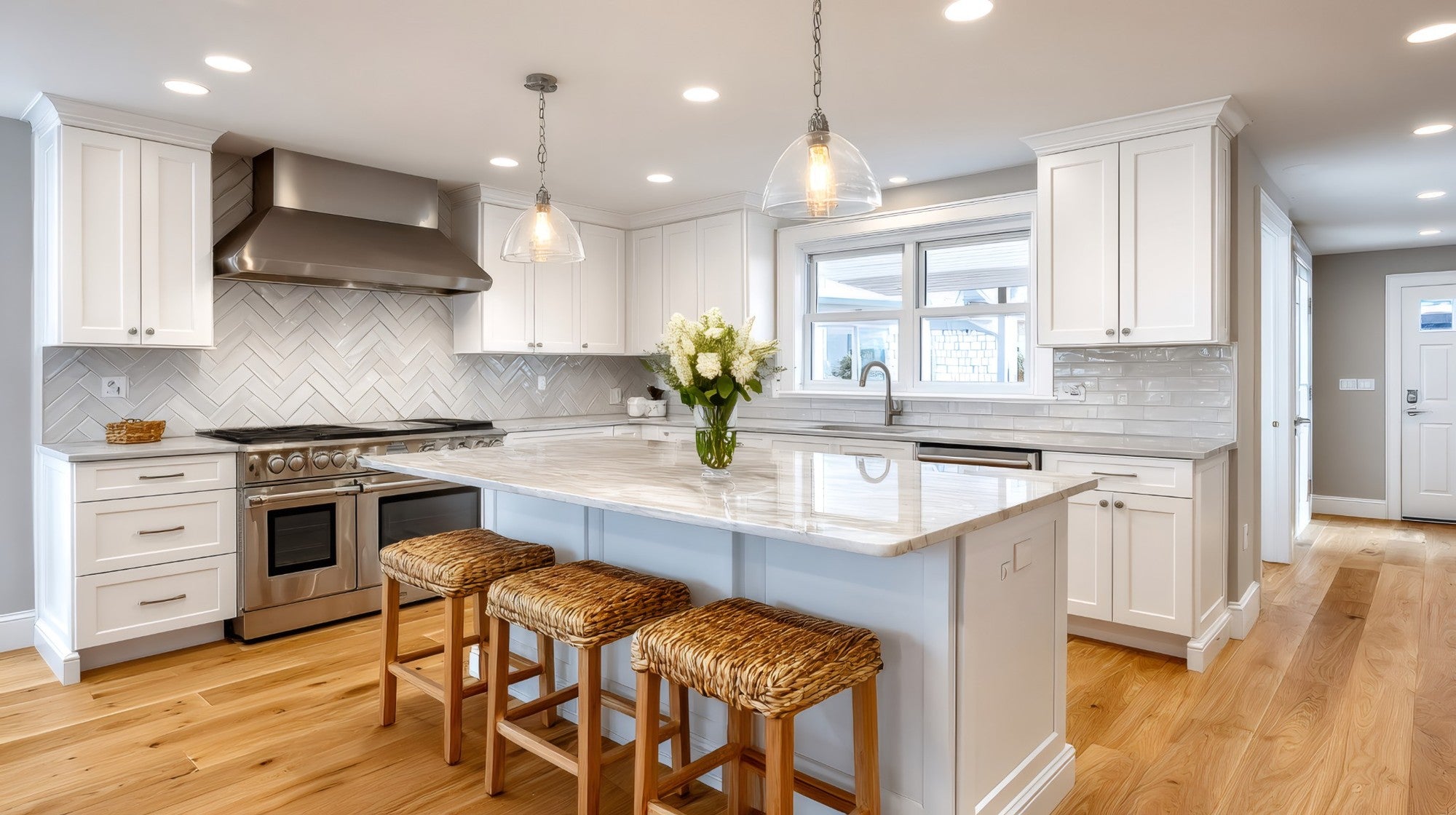 Legacy White Shaker kitchen with large island, marble countertops, stainless range hood, and natural oak flooring